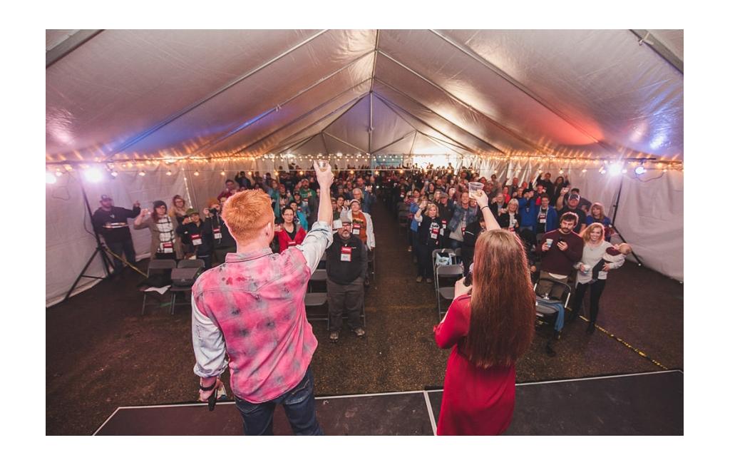 Heath and Alyssa standing on stage toasting to a large crowd of people