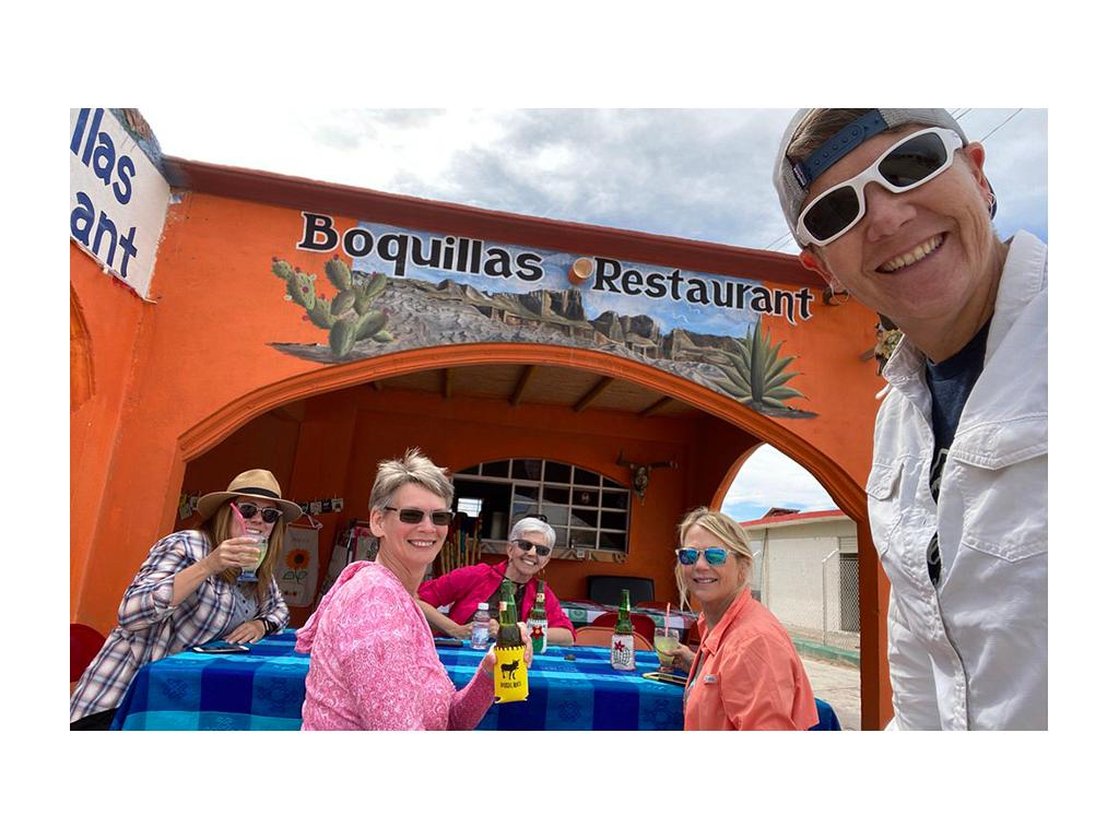 Noel taking a selfie with four friends in background sitting at table outside of Mexican restaurant