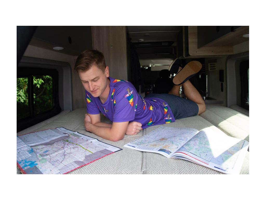 Mikah laying on bed planning route with two paper maps