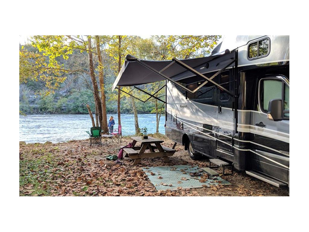 Navion parked at campsite near water with awning extended