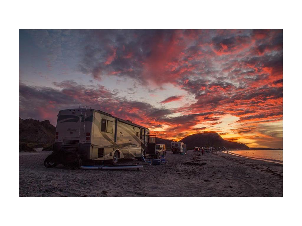 Journey parked on beach with colorful sunset and mountains in distance