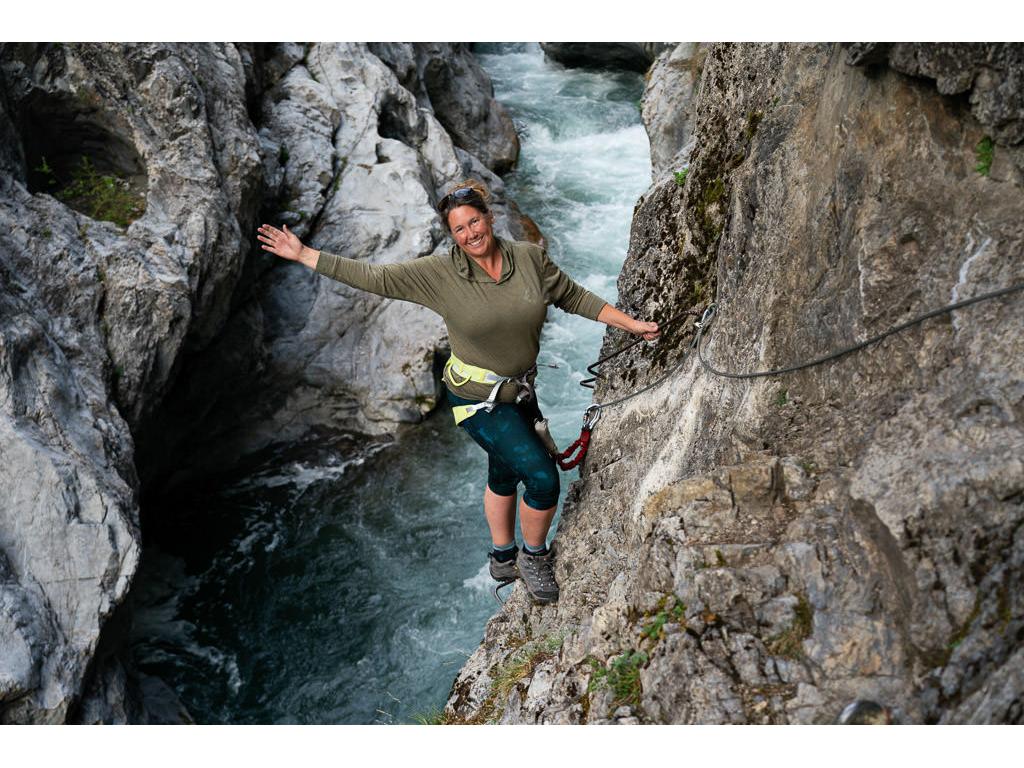 Kathy leaning back on a climb down a cliff side with a river below her