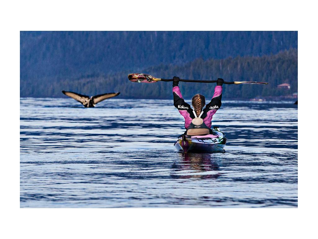 Abby kayaking and holding up paddle with large bird flying nearby