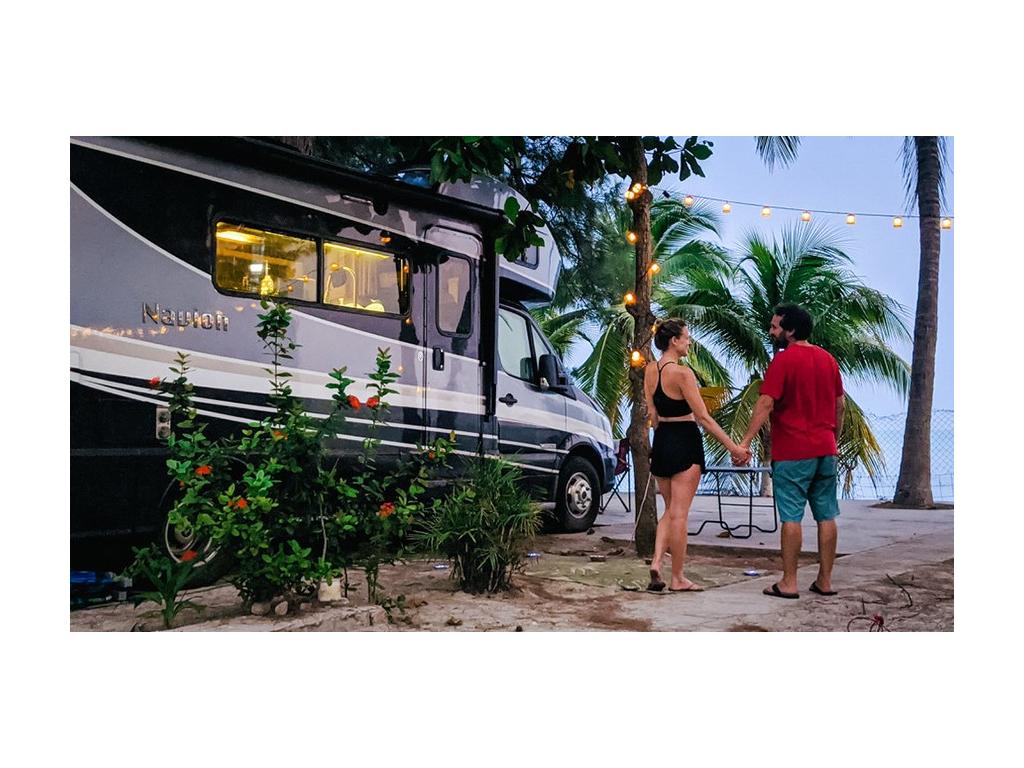 The Newstate Nomads holding hands next to Navion parked on beach