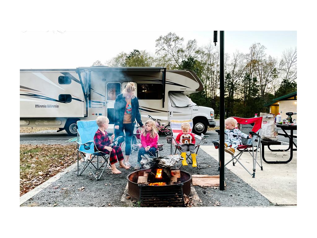 Tera and kids sitting around a fire with Minnie Winnie in background.