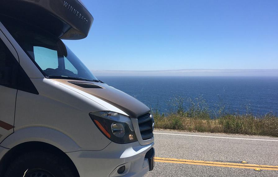 Front end of Winnebago View driving down road with view of ocean