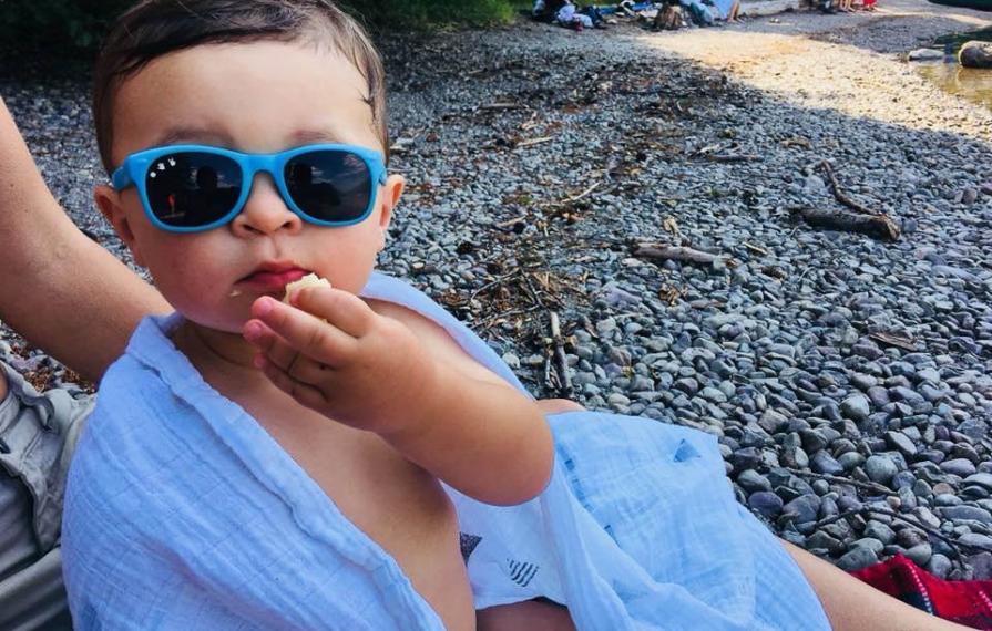 Caspian wrapped in a blanket wearing sunglasses eating a snack