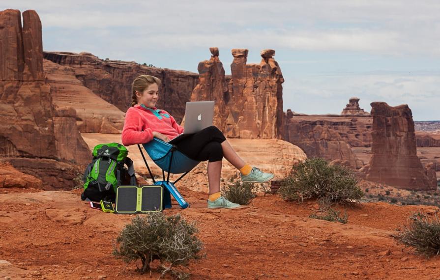 Abby sitting in chair doing homework on laptop with red mountains in background