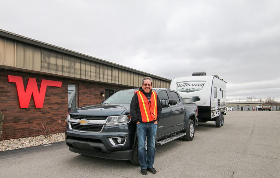Traveling Robert standing in front of Winnebago Towables plant with truck pulling trailer