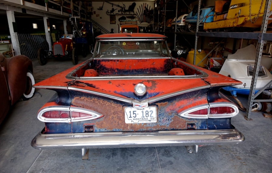 Old red car among other old vehicles in storage building.