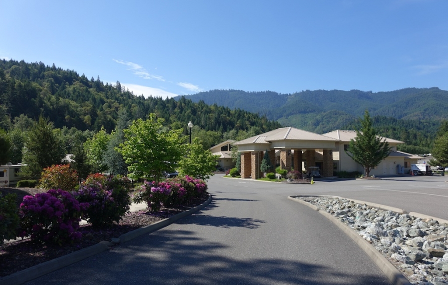 Canyonville entrance lined with flowers in a beautiful tree covered hillside area.