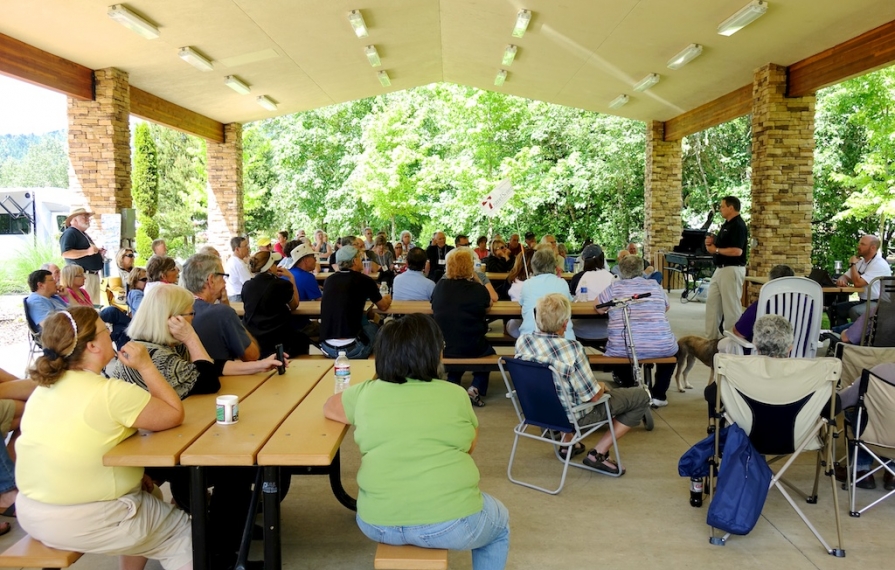 Group gathered under covered picnic area listening to a speaker.
