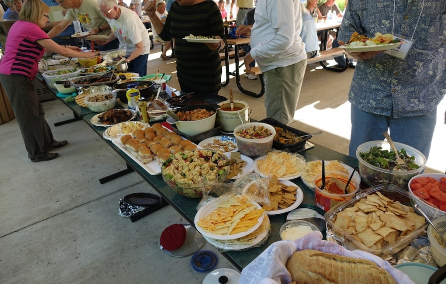 People lined up getting food from a potluck style meal.
