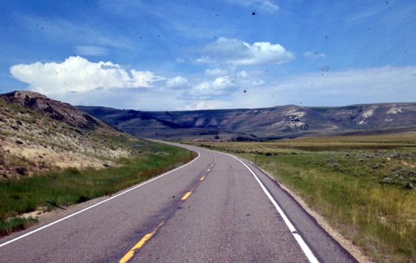 Road curving towards the mountains ahead with blue sky above.