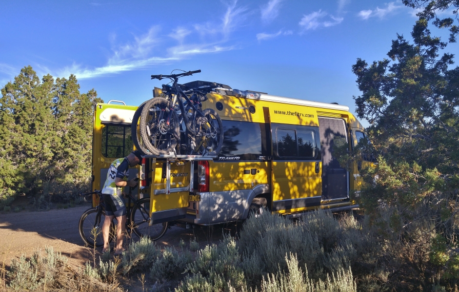 James getting bike from the back of their Winnebago Travato parked among trees.