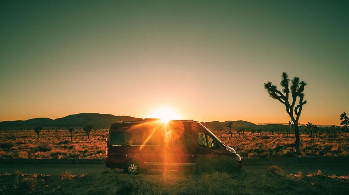 Winnebago Travato with sun setting over the mountains in the background.