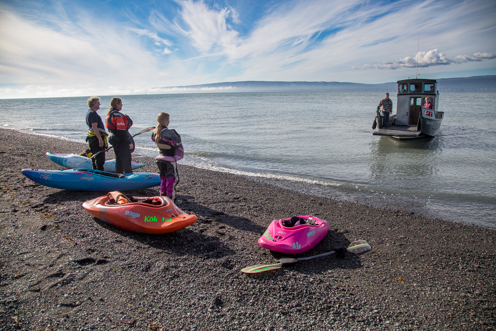 Water taxi heading towards people and their kayaks waiting on the shore.