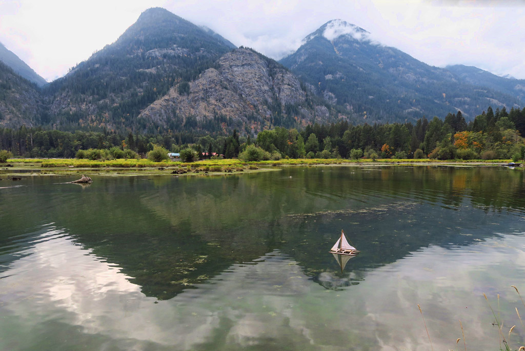 Small toy boat on the water beneath mountains.