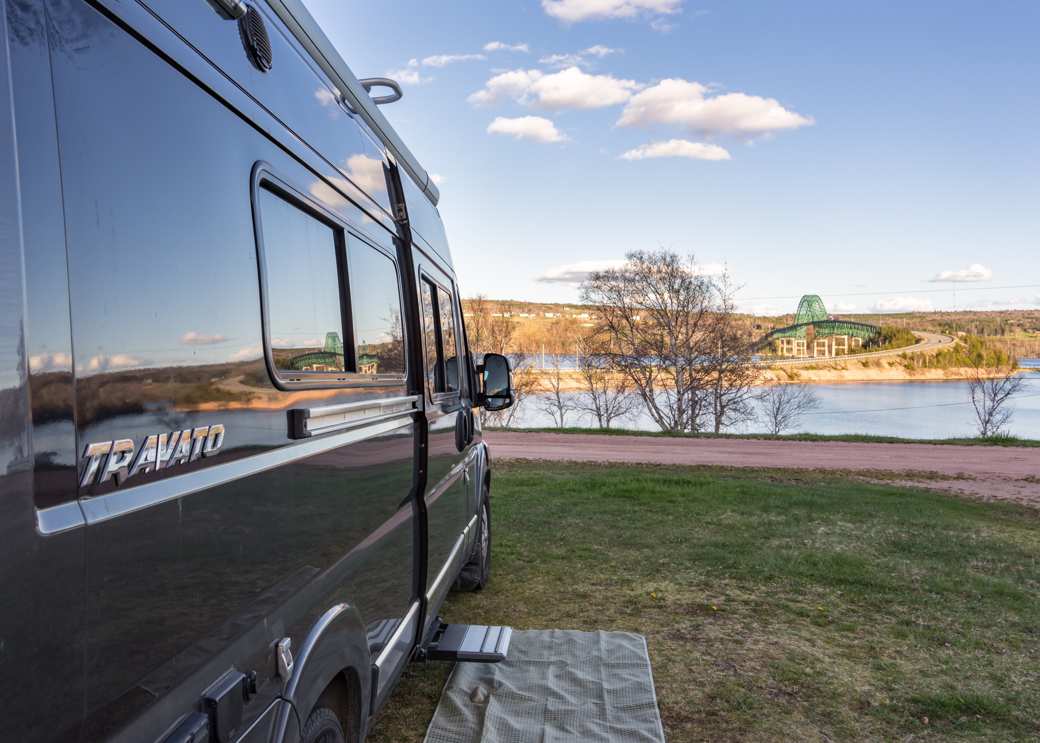 Winnebago Travato parked on the grass looking out at water ahead.
