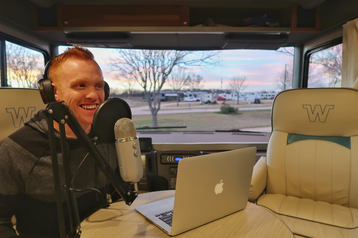 Heath talking in to a mic while working on laptop at optional coffee table between driver and passenger seat.
