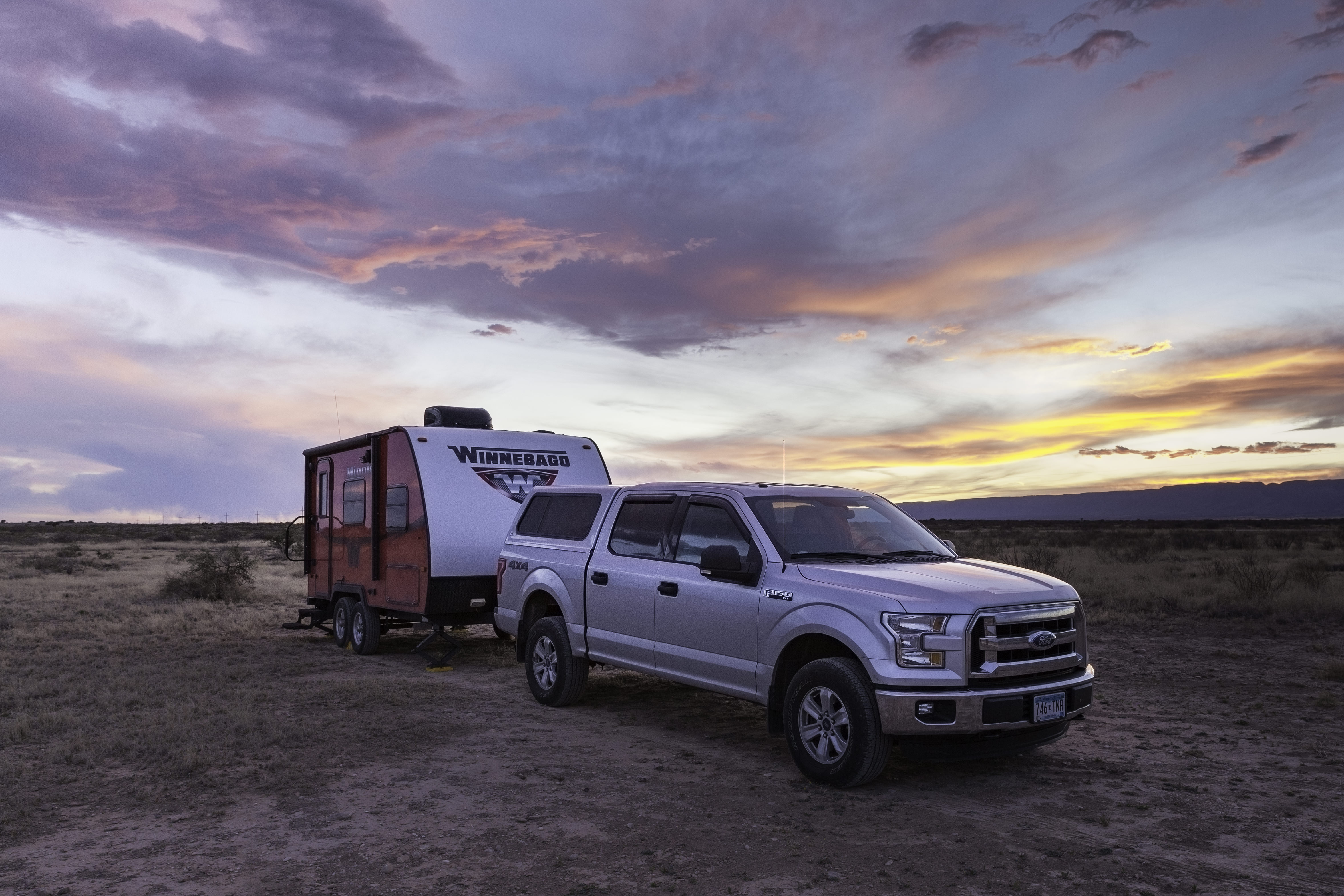 Truck with Winnebago Minnie attached with colorful sunset above.