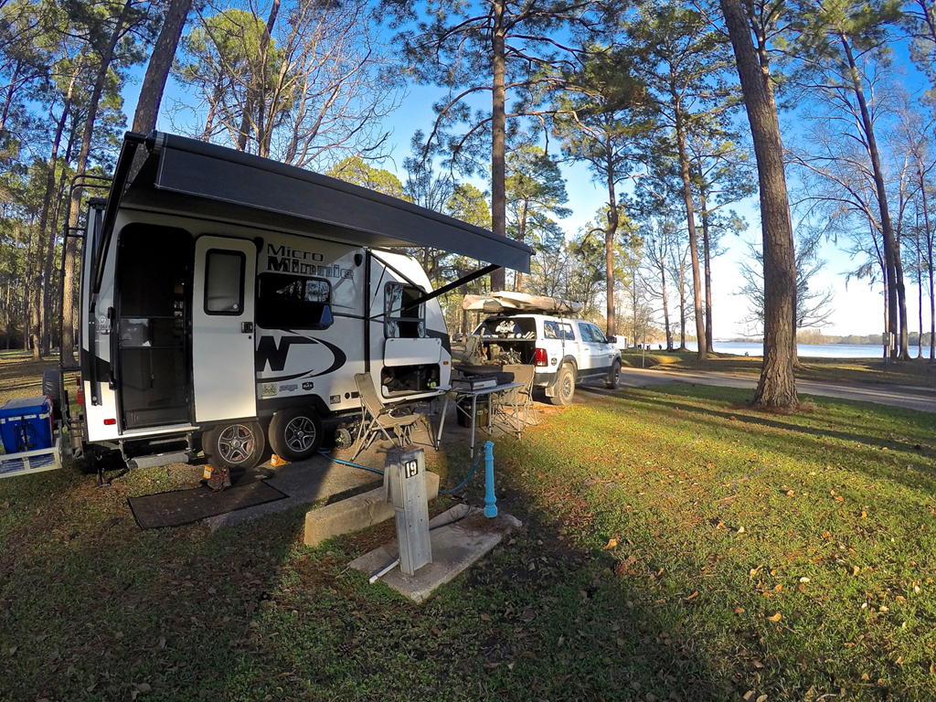 Winnebago Micro Minnie in campsite beneath trees and along the water.