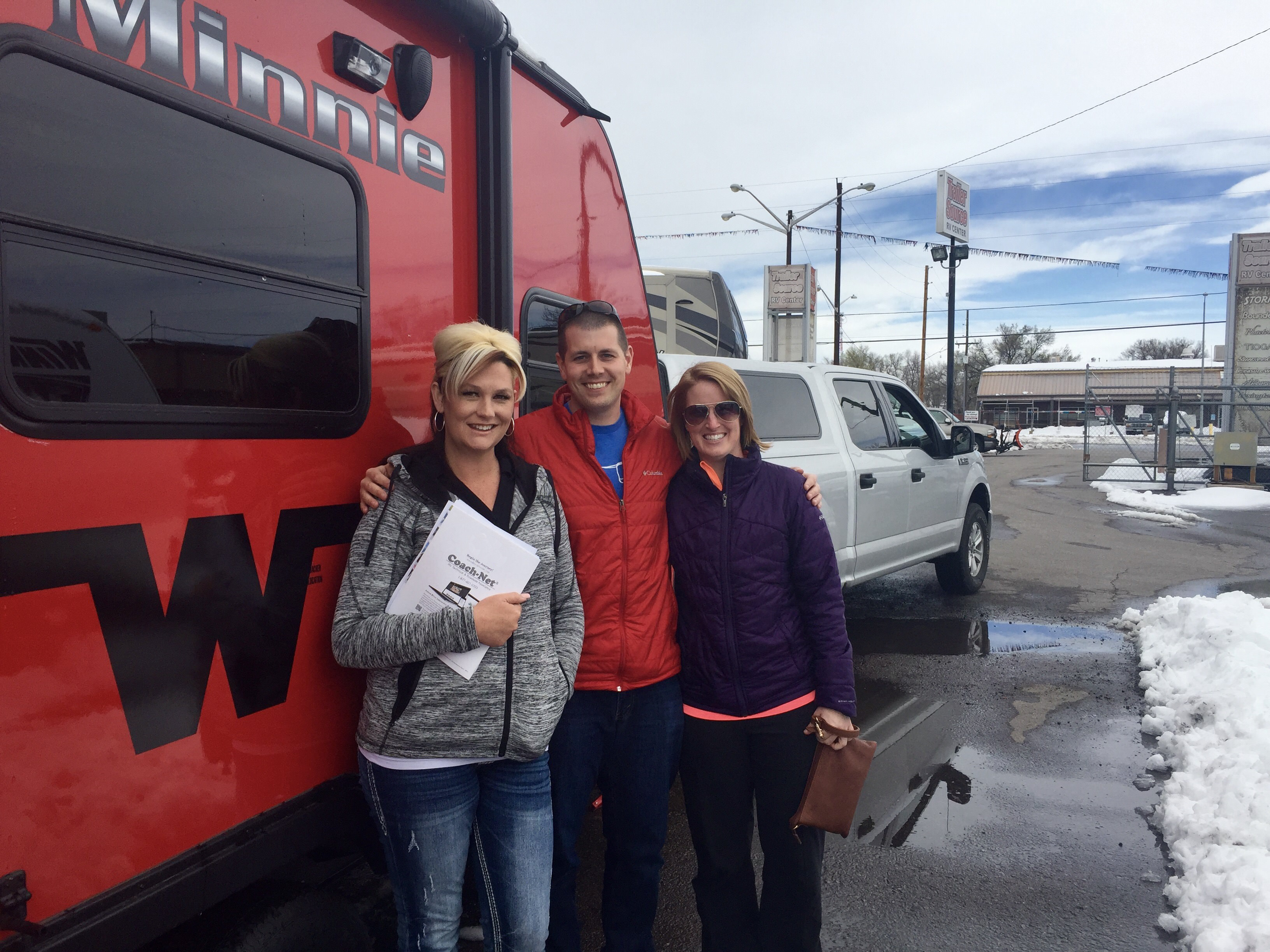 Couple with RV saleswoman standing outside their Winnebago Minnie.
