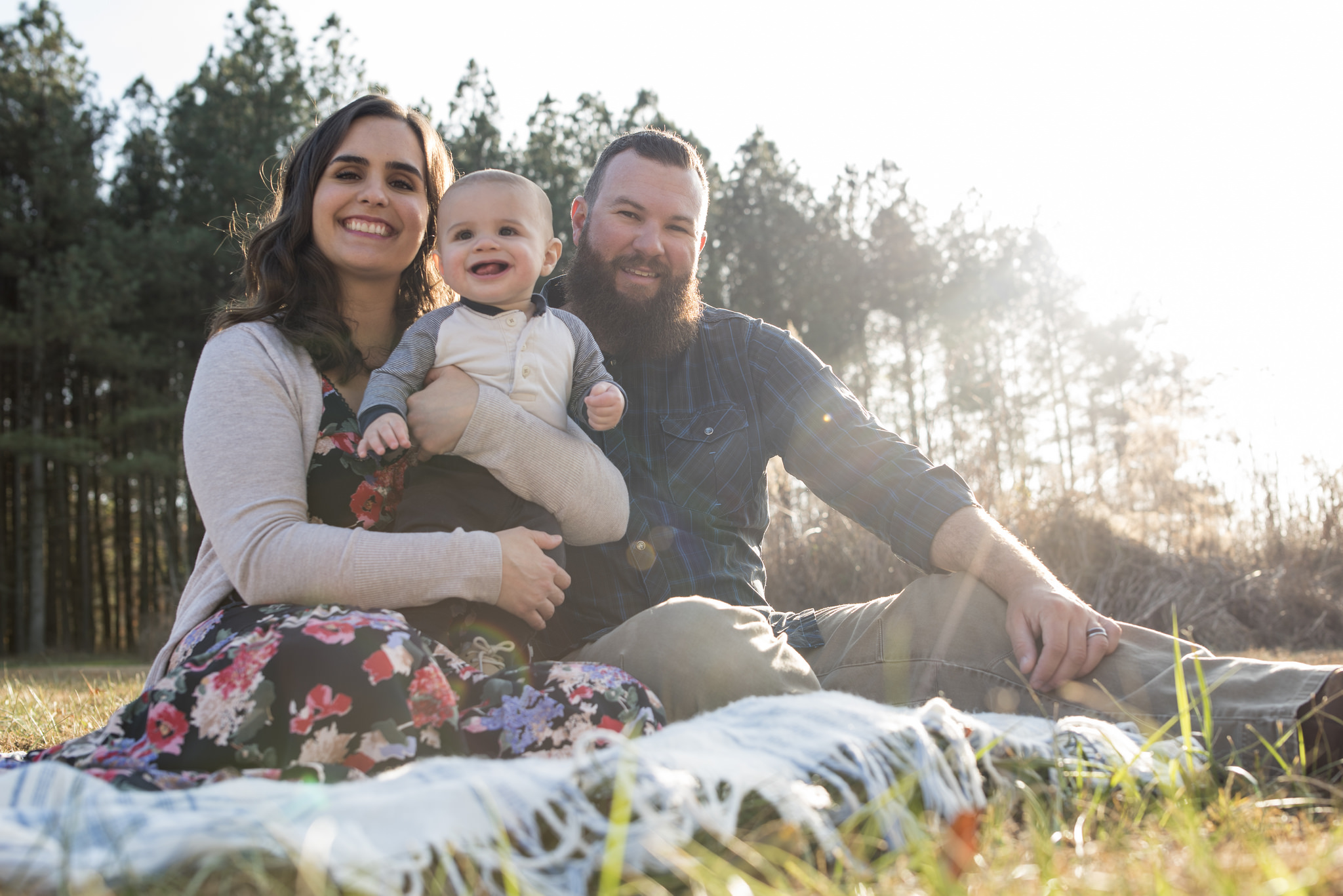 Family of three smiling while sitting in the grass.