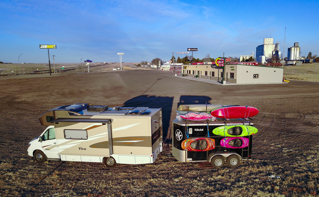 Winnebago View with trailer attached parked at a gas station in the middle with very little nearby.