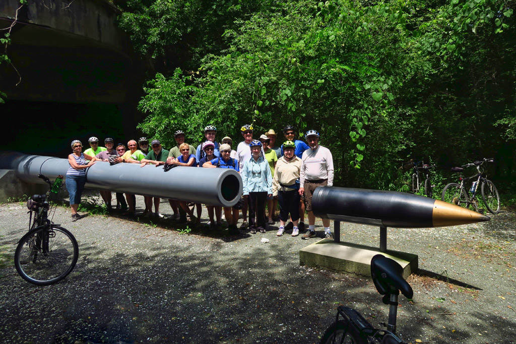 Group of people wearing bike helmets gathered by the WWII gun barrell used on the U.S.S. Missouri.