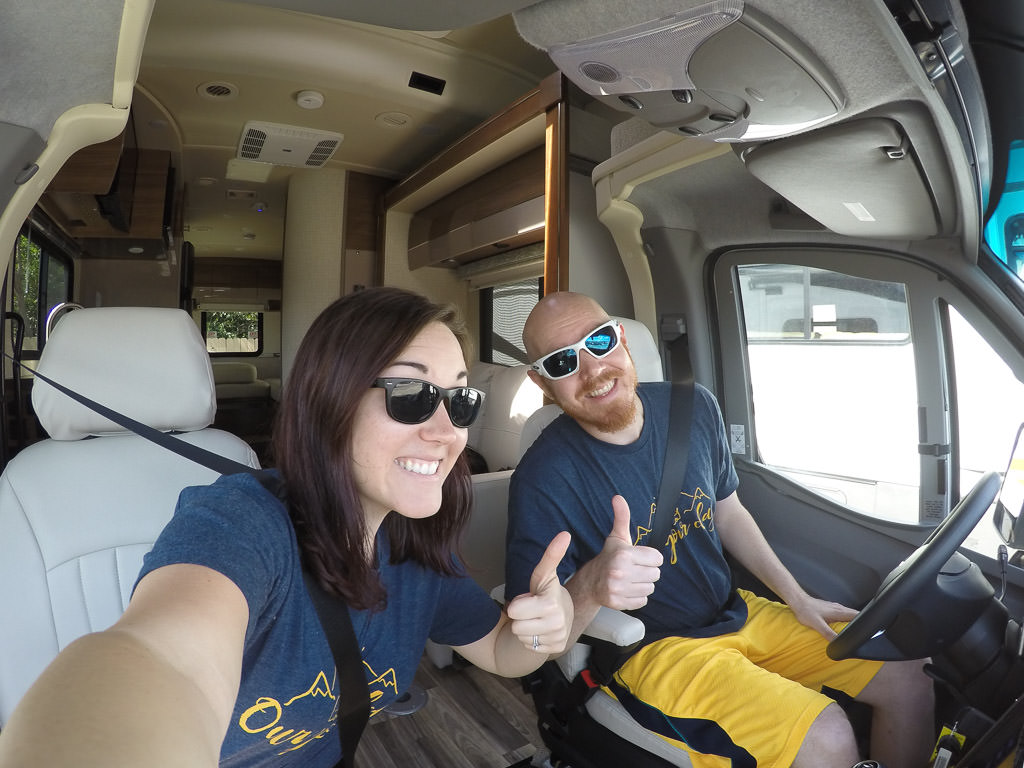 Couple sitting in front seats of Winnebago View with thumbs up.