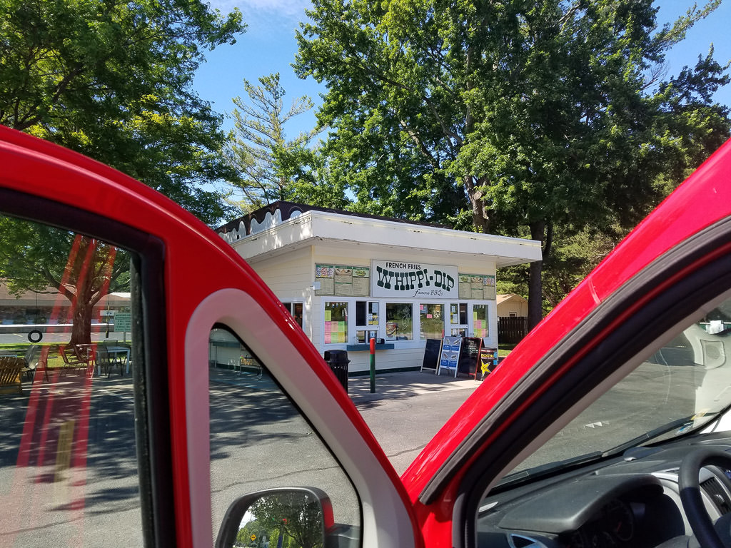 Red Winnebago Travato pulled up and parked in front of a Whippi-Dip.