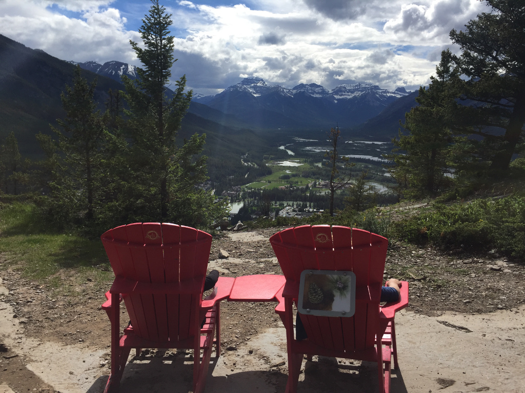 People in chairs overlooking the Tunnel Mountains in the distance with water running in the valley below.