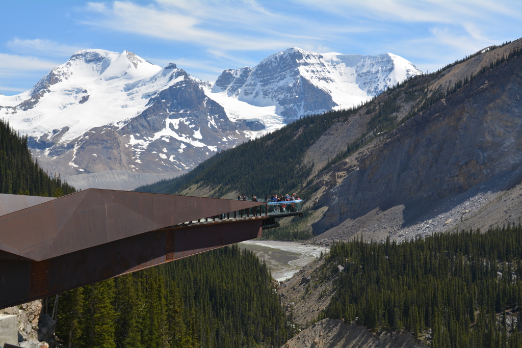 People standing out on a glass bottom skywalk over the edge of a mountain.