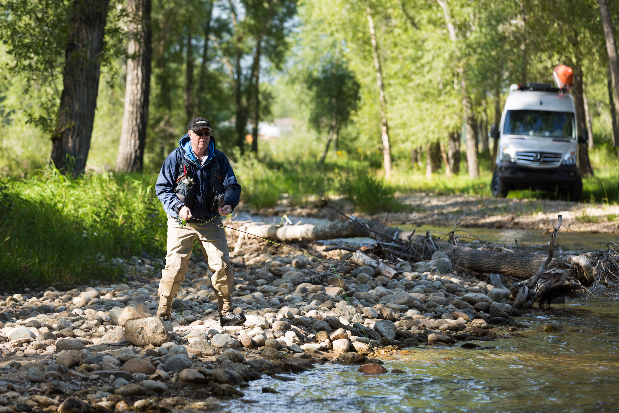Man on the rocks fishing with Winnebago Revel parked just behind him.