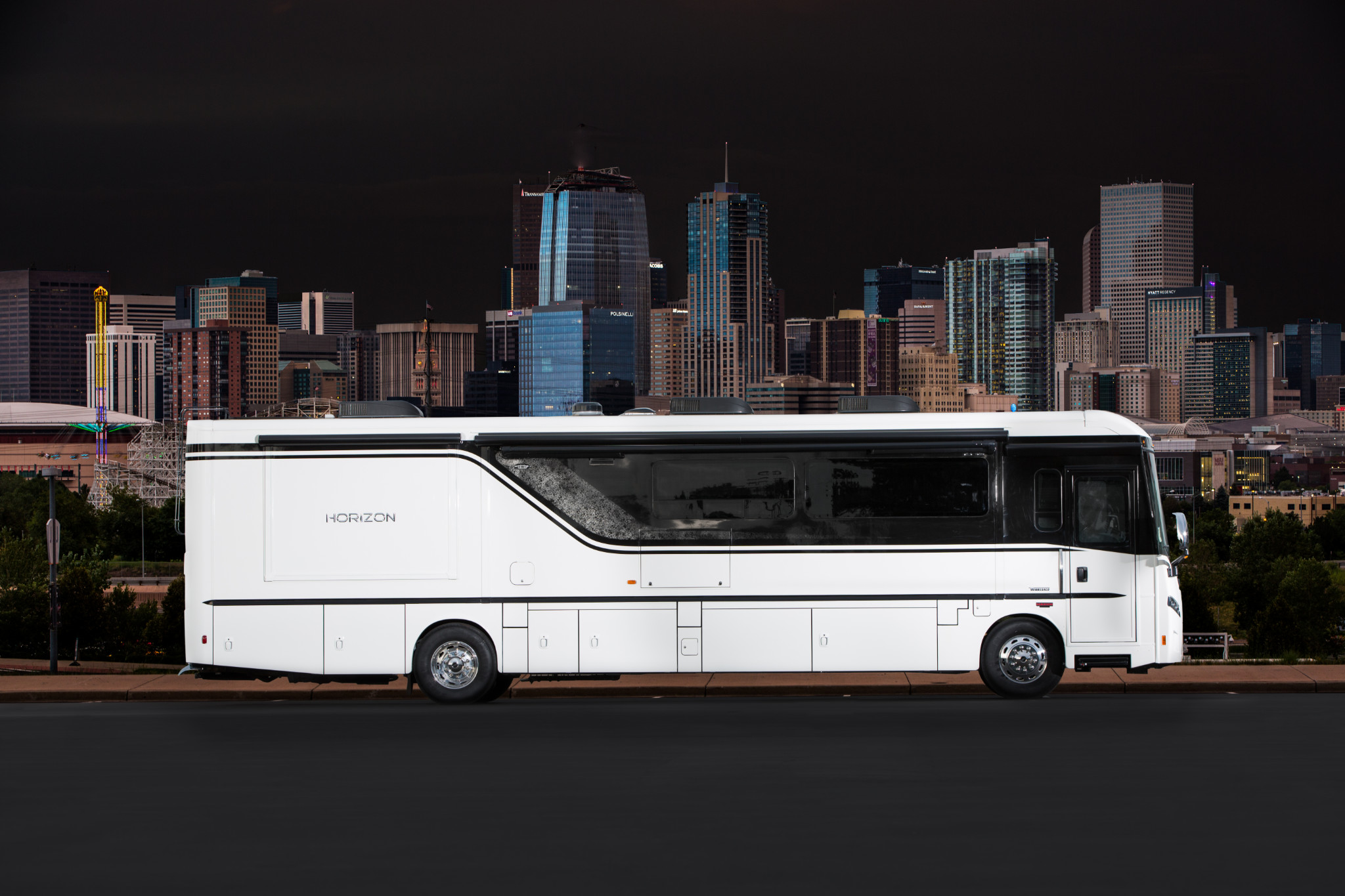 Winnebago Horizon parked in parking lot with city skyline in the background with dark night sky overhead.