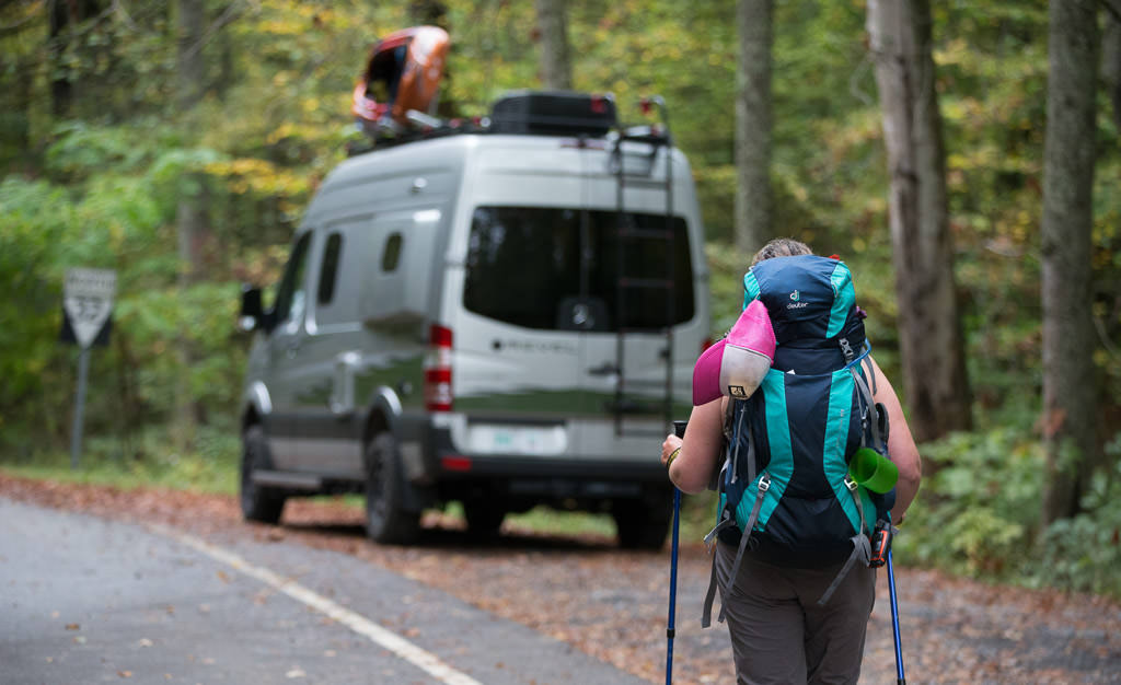 Woman hiking back towards Winnebago Revel parked along side a road.