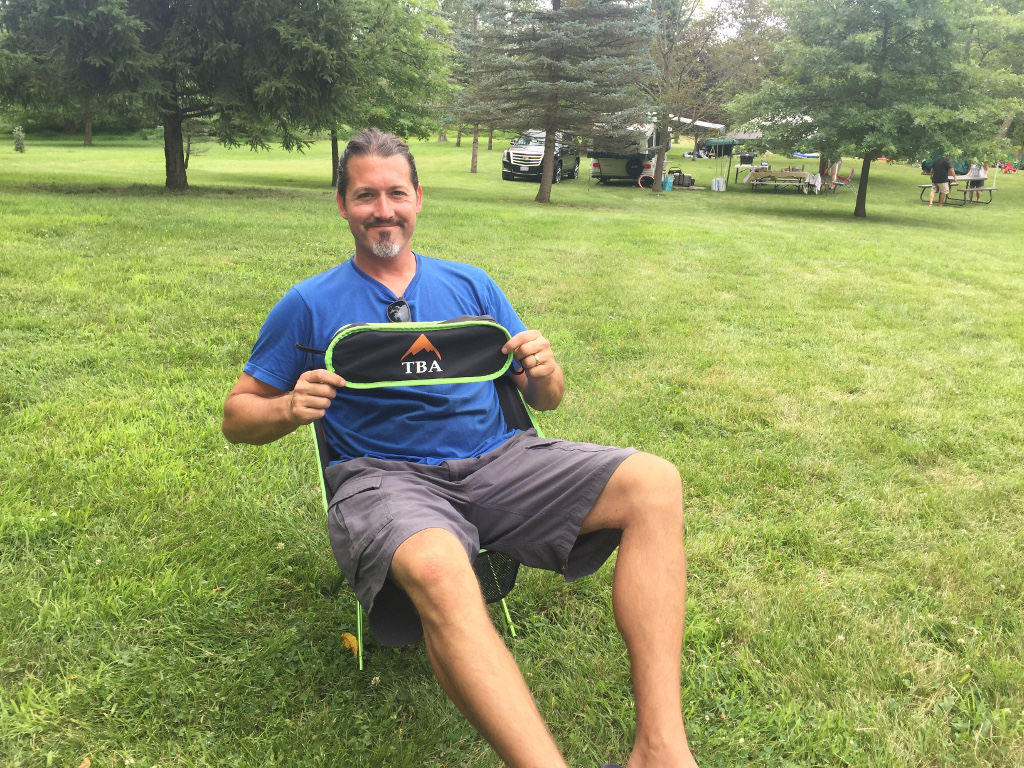 Craig sitting in chair holding up bag to Tiny Big Adventure chair
