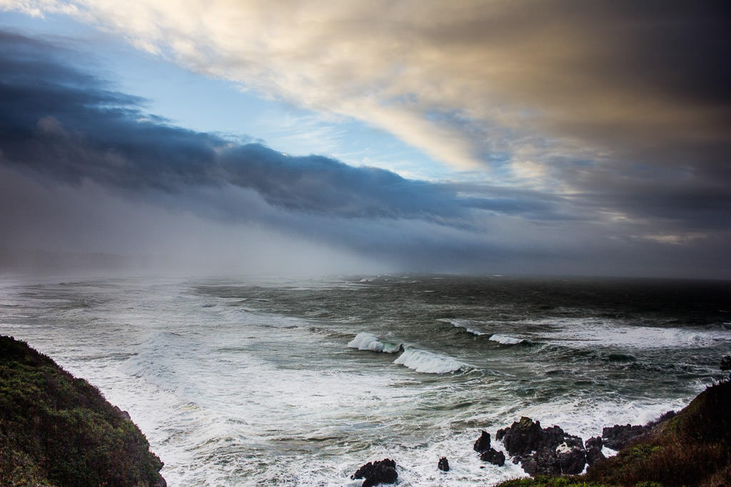 Ocean water rolling over rocks with colorful sky up above