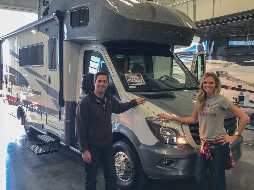 Dan and Lindsay standing outside their Navion with a sold sign in the front window.
