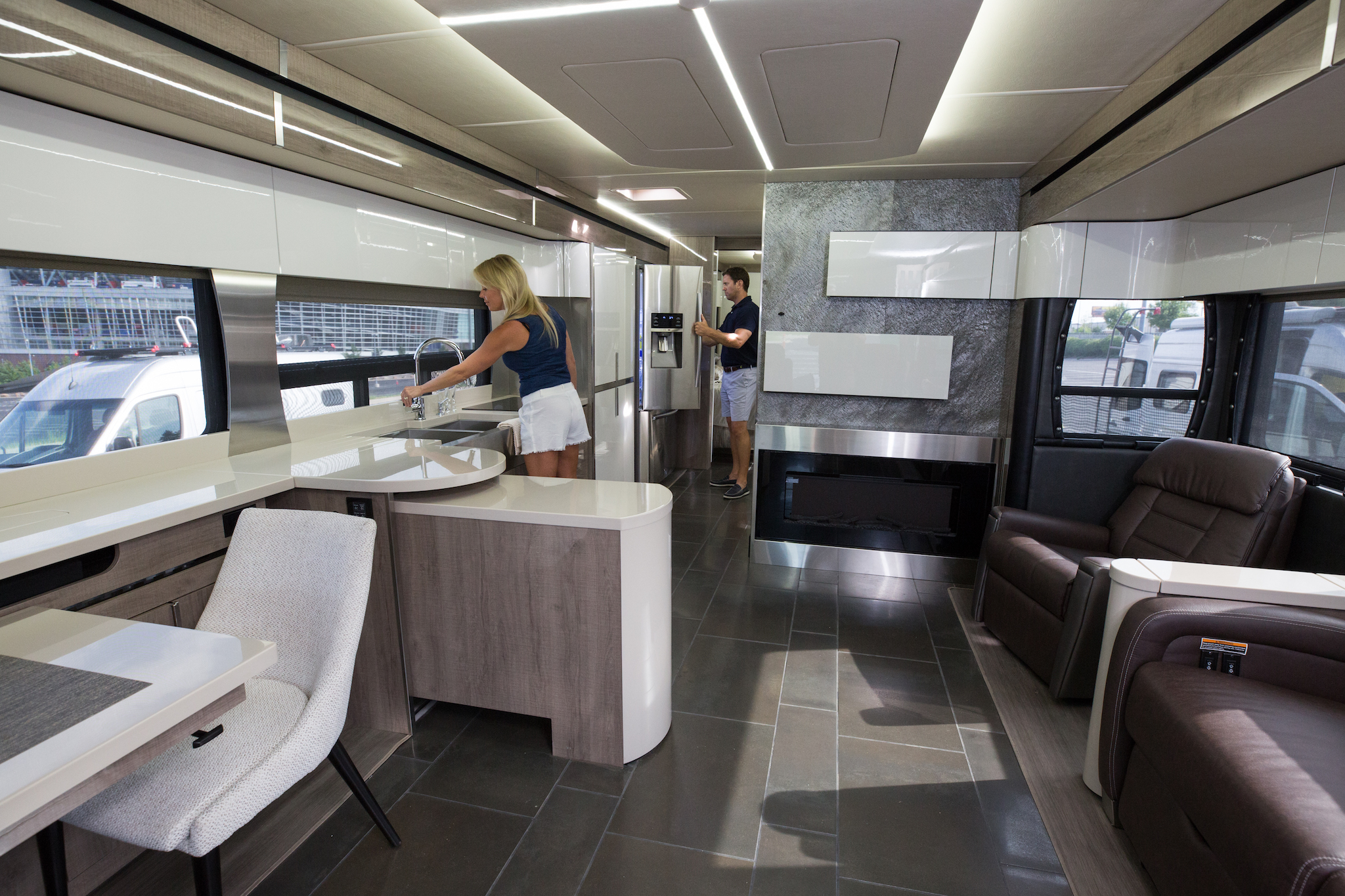 Woman using the kitchen sink, and man looking in the fridge of the Winnebago Horizon.