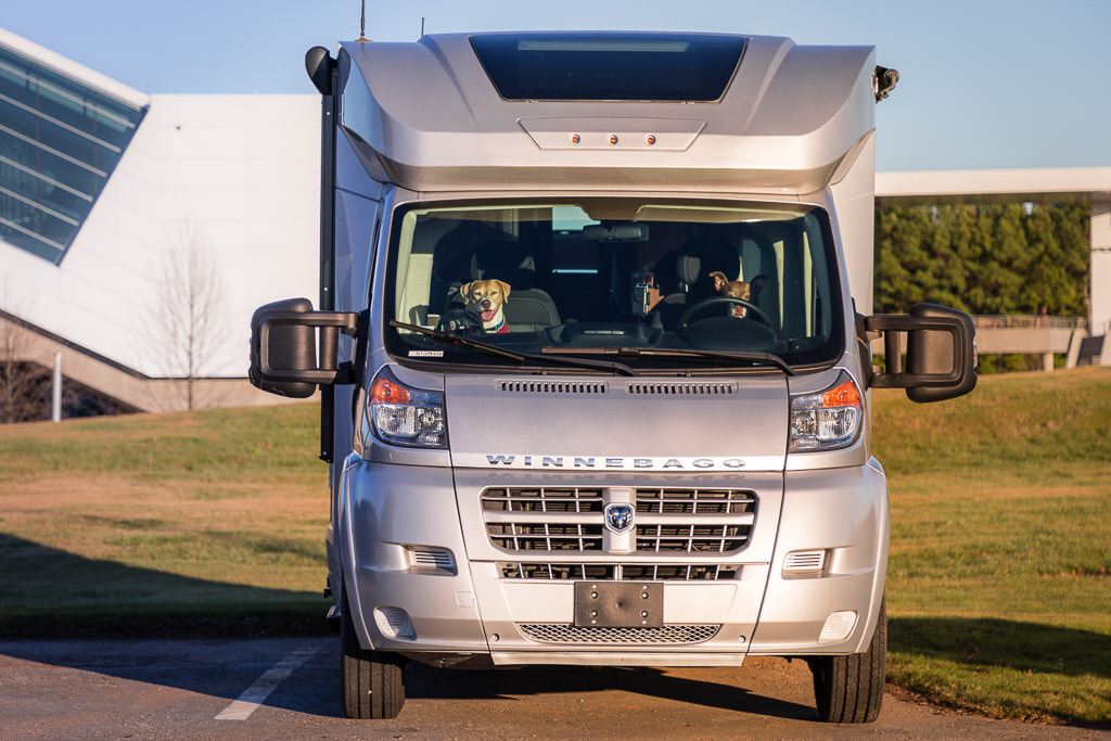 Dogs sitting in the driver and passenger seat of parked Winnebago Trend.