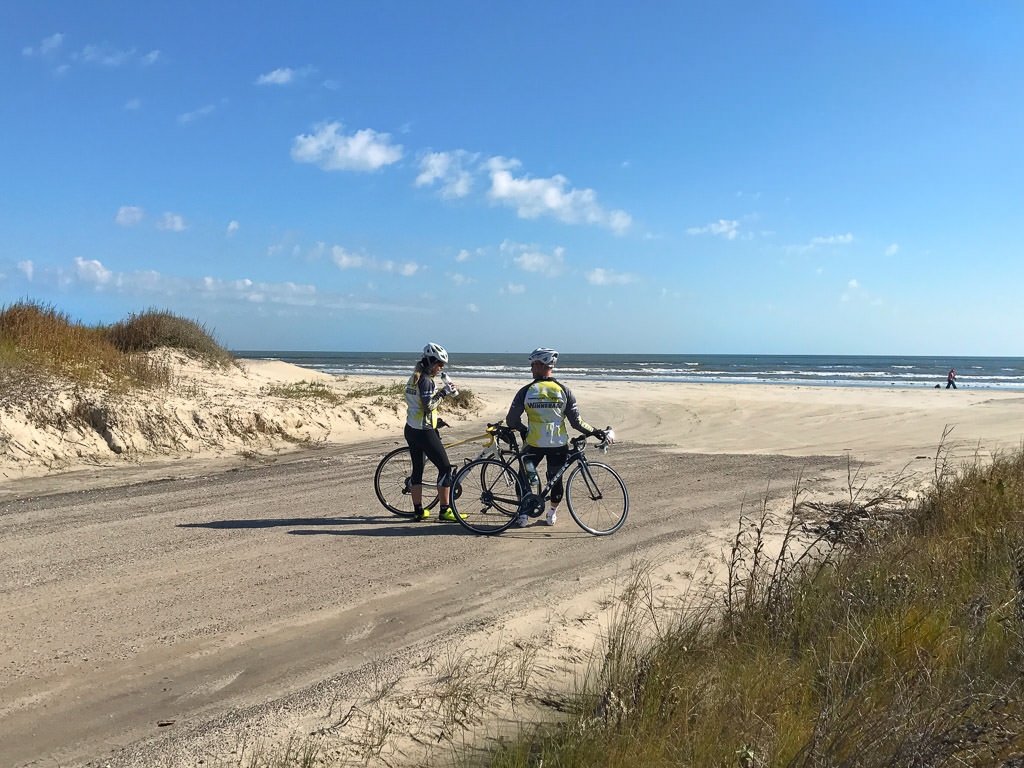 Stef and James standing next to beach taking a break from riding bikes