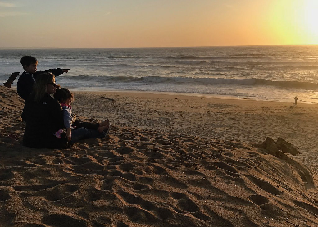Mom and kids sitting on sandy beach looking at the ocean