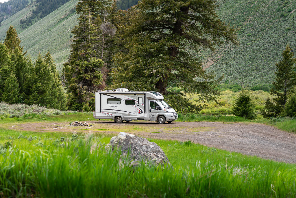 Winnebago Trend parked with trees and green steep hills in the background
