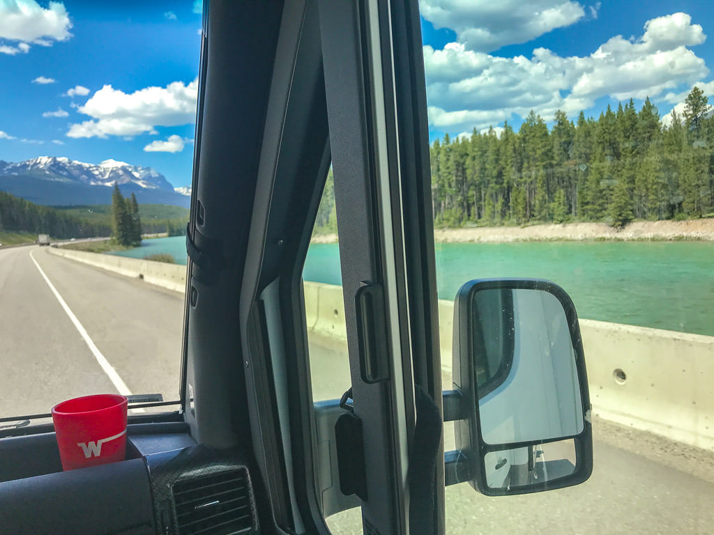 Driving RV down the highway with mountains ahead and water and trees to the right