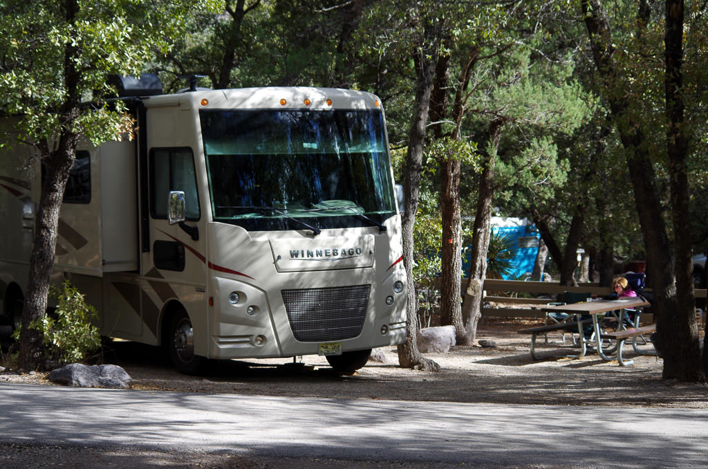 Winnebago motorhome parked at campsite between trees.
