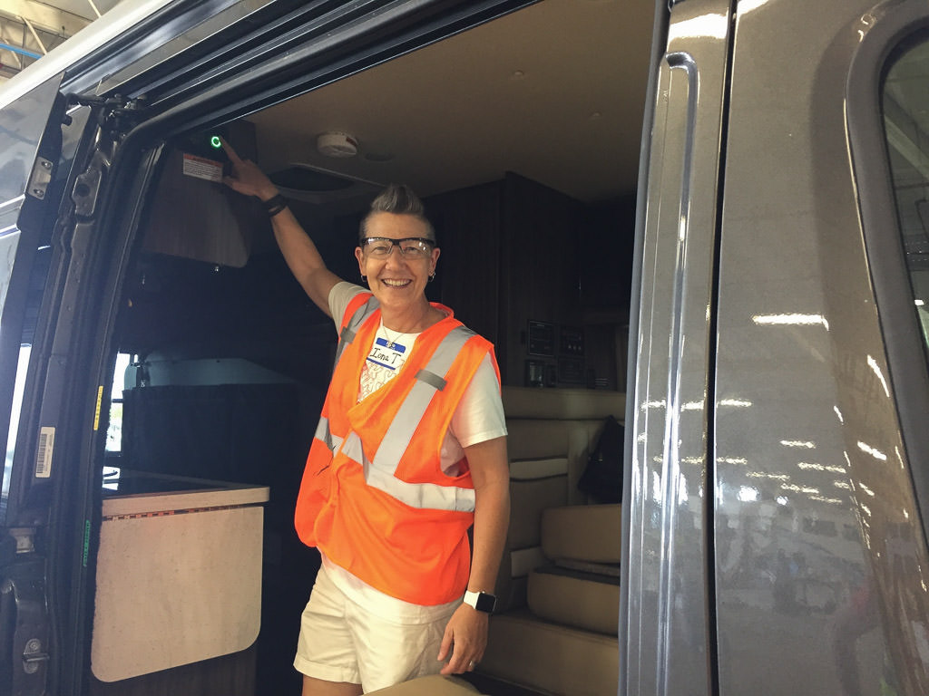 Woman with a bright orange safety vest on standing inside Winnebago Travato. 