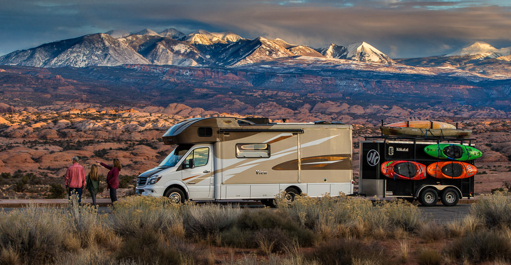 Winnebago View parked with mountains in the background and a trailer with kayaks attached to the side.