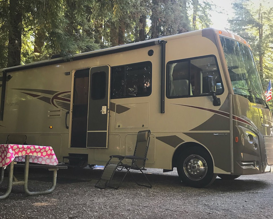 Winnebago Vista parked in campsite with picnic table and lounge chair outside.